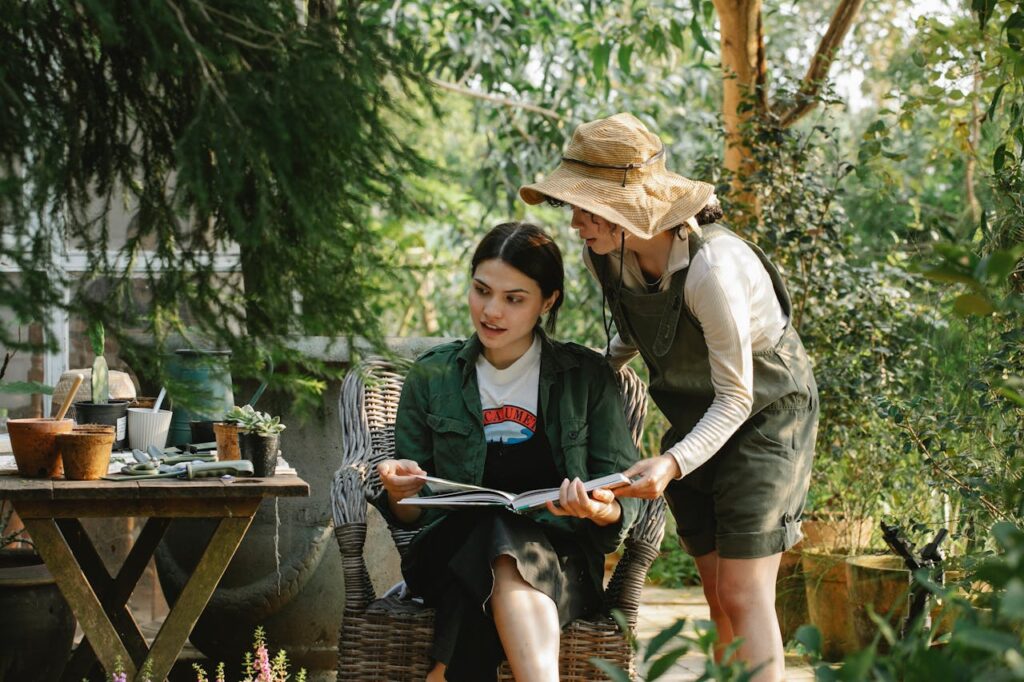 Young multiracial female horticulturists with textbook speaking against assorted succulent plants in pots in summer garden