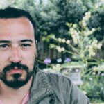 Portrait of a young man with facial hair, outdoors in a natural setting. Serious expression.