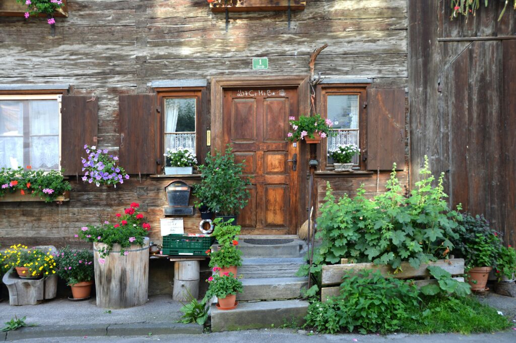 farmhouse-summer-holiday-holiday-summer-159869-159869 Charming rustic house entrance with wooden door and colorful flower pots creating a vibrant scene.