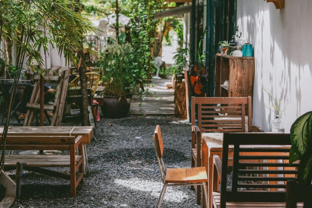 pexels-photo-10165389-10165389 Inviting outdoor garden seating area with wooden tables and chairs, surrounded by lush greenery.