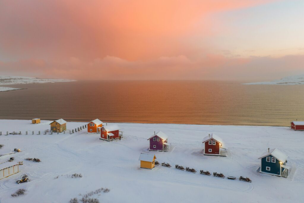 pexels-photo-6882084-6882084 Aerial view of colorful cabins in snowy Pechengsky District, Russia, during a stunning winter sunset.