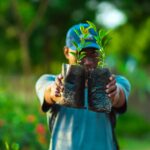 African man in Abuja holding saplings in a garden, promoting greenery and growth.