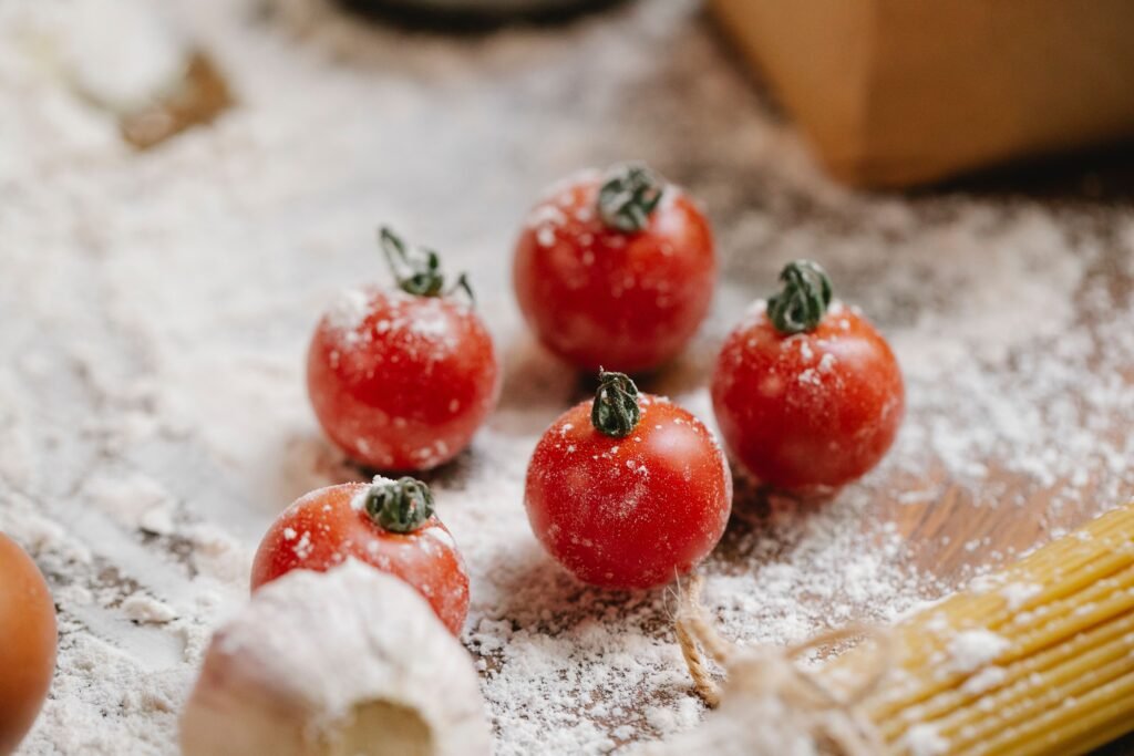 From above of ripe red cherry tomatoes with garlic and raw spaghetti on wooden table with flour