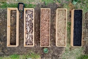 Top view of wooden boxes with piles of firewood wood chips sawdust and coal placed on ground in agricultural plantation